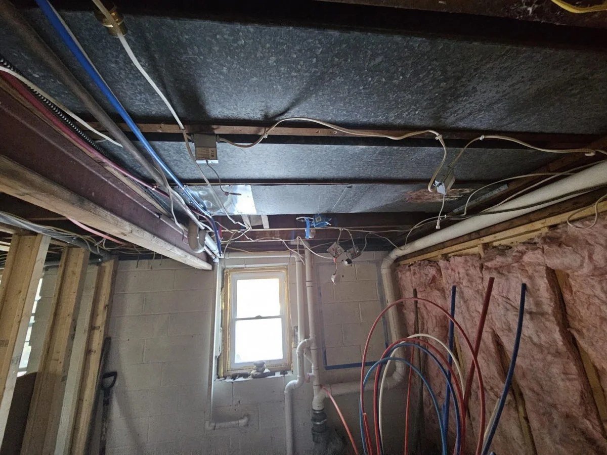 A New Life Spaces basement bathroom corner before work: concrete block walls, a small window, exposed plumbing and insulation.